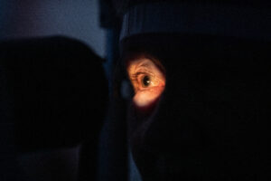 Close up image of an older woman having an eye test. Her face is obscured by darkness wiht a bright ly lit circle around one eye.