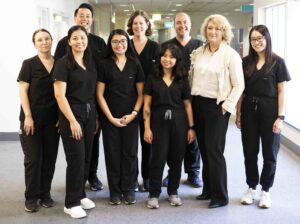 A group of nine Cerulea Clinical Trials staff standing in a corridor. They are all wearing black scrubs with the exception of CEO Michelle Gallaher who is wearing a cream shirt and jacket with black trousers.