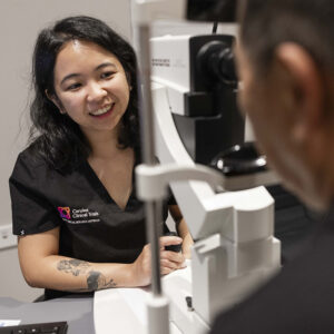 A clinician operates specialised eye examination equipment while consulting with a patient.