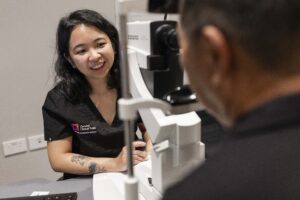 A clinician operates specialised eye examination equipment while consulting with a patient.